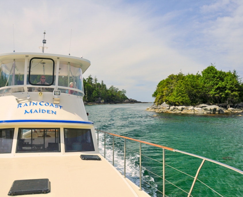 Front view of boat with captain at helm with green ocean water and islands in background