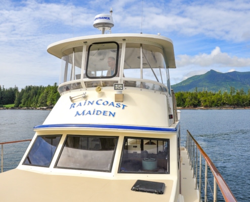 Front view of upper deck of luxury yacht with tree covered shore line and mountains in distance
