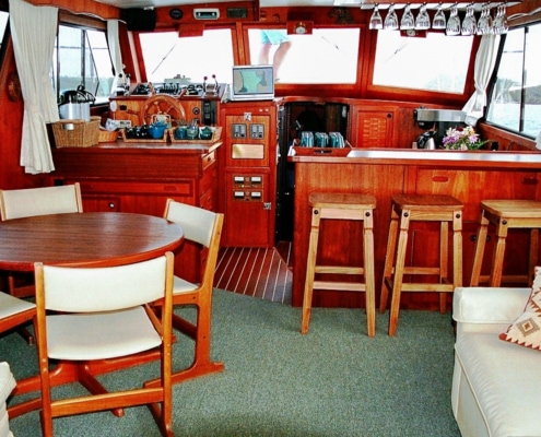 Inside luxurious saloon of motor yacht, showing bar counter, table and chairs, couch, lower helm